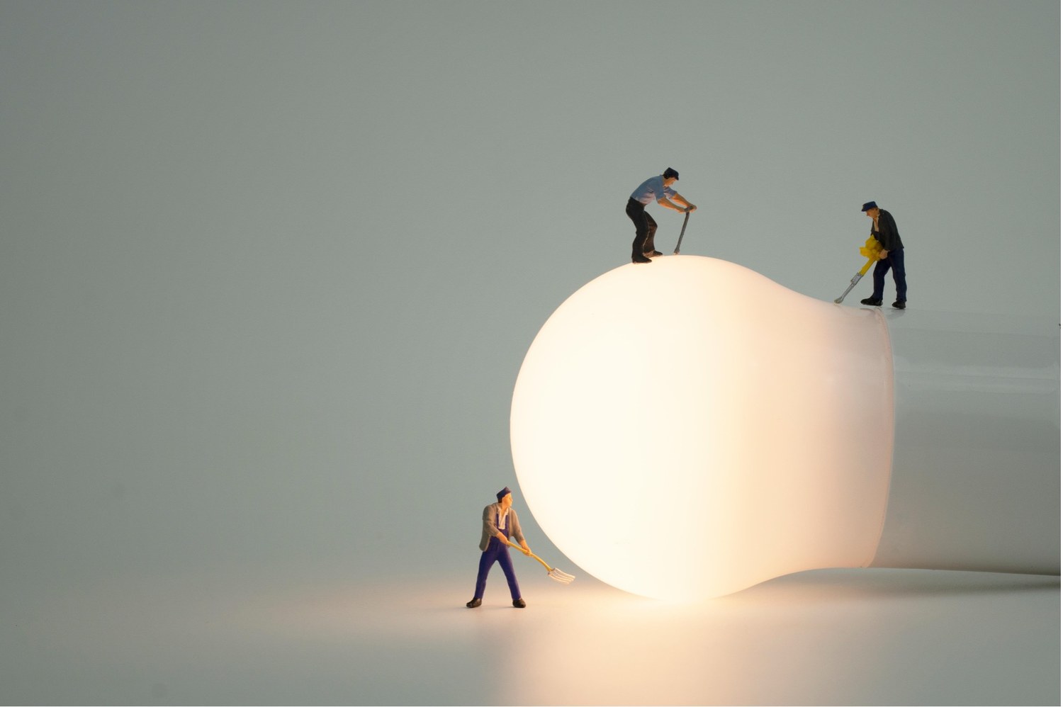 Miniature figures working around a large illuminated bulb, representing making a commercial system visible